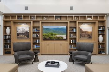 A living room with two chairs, a table, and a bookshelf with pictures on it.
